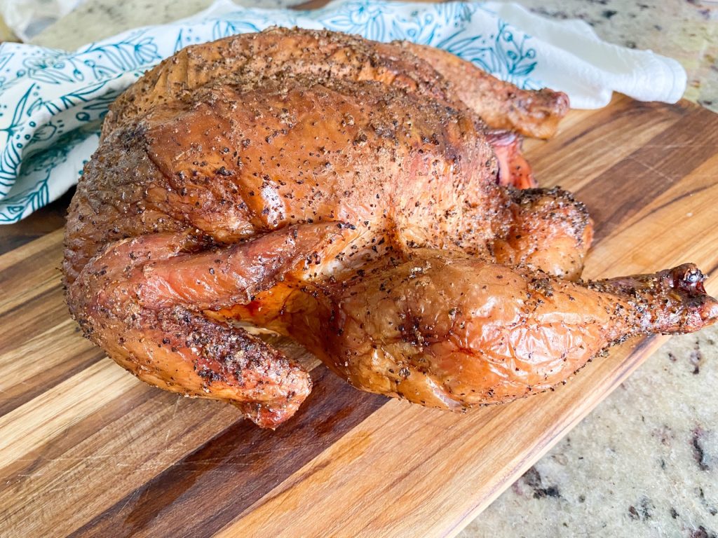 A crispy smoked whole chicken sitting on a wooden cutting board